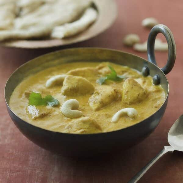 Bowl of creamy korma chicken with coconut, cream, and cashew nut sauce, garnished with herbs.