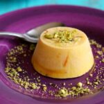 Kulfi, Indian ice cream with nuts and raisins on a purple dish, garnished with chopped pistachios.