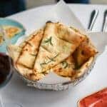 Golden-brown butter-toasted bread garnished with rosemary in a crystal bowl, served on a dining table.